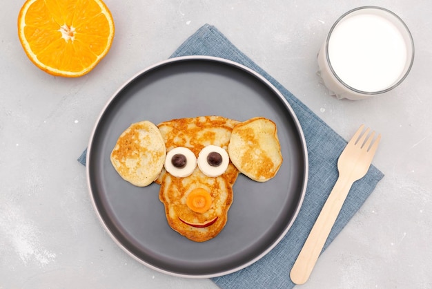 Bocadillo divertido con forma de cara de mono de panqueque con queso en un plato Dulce de postre saludable para niños lindos para niños Arte de comida para el desayuno y el almuerzo con manzanas sobre fondo de hormigón grisvista superior