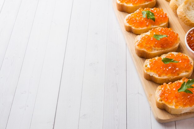 Bocadillos con el caviar de los salmones rojos en un tablero de madera. Sobremesa blanca.