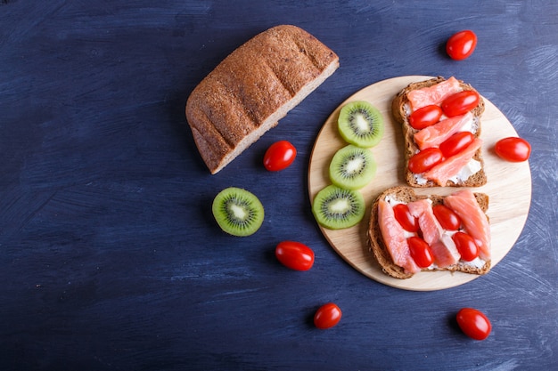 Bocadillos de color salmón ahumados con mantequilla en fondo de madera oscuro.