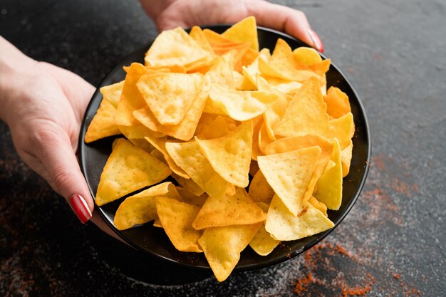 Bocadillos de comida rápida poco saludables. malos hábitos alimenticios. manos de mujer sosteniendo crujientes nachos deliciosos en un plato.