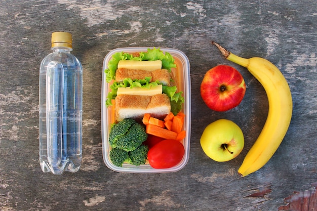 Bocadillos, frutas y verduras en caja de comida, agua.