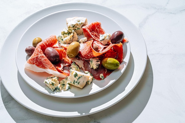 Bocadillos italianos tradicionales jamón aceitunas y queso azul jamón picado con una variedad de aceitunas en escabeche y trozos de queso azul caro junto a una copa de vino fresco