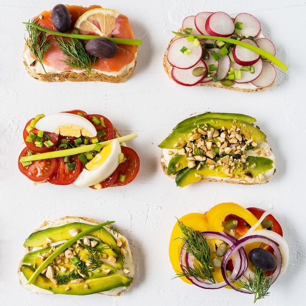 Bocadillos o tapas preparados con queso crema, verduras y salmón, sobre fondo blanco.