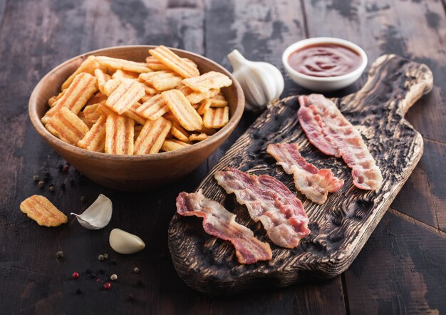 Bocadillos con sabor a tocino con lonchas de tocino a la parrilla sobre una tajadera vintage con ajo y salsa sobre fondo de madera.