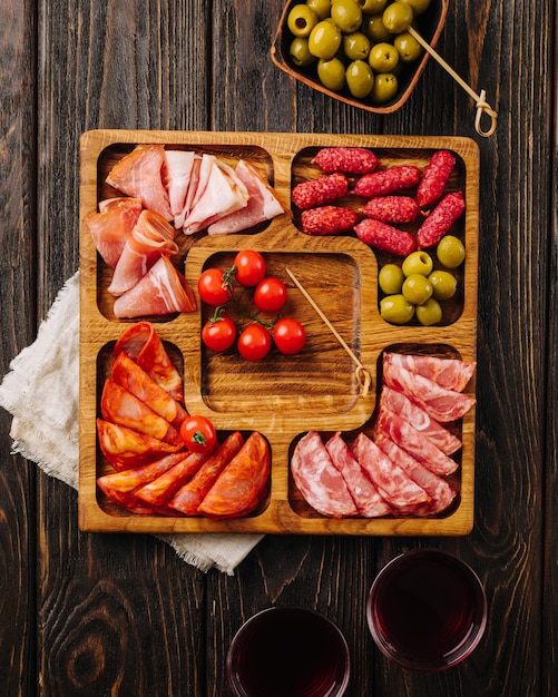 Bocadillos para vino en una tabla de madera menazhnitsa con salchichas, aceitunas y tomates cherry