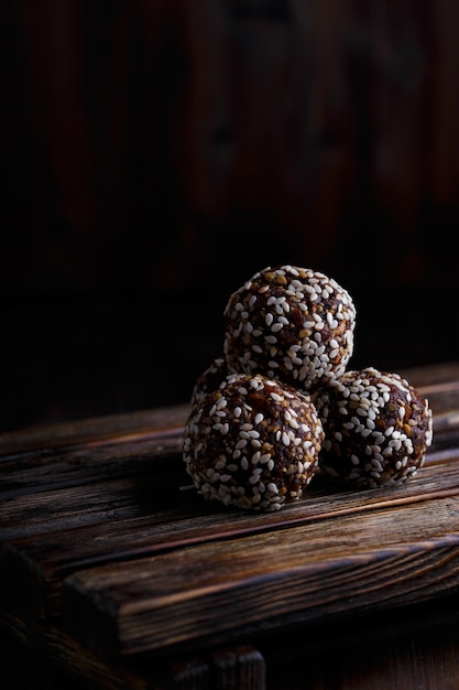 Foto bocados vegetarianos orgánicos de energía saludable con nueces, dátiles, miel y sésamo sobre madera oscura