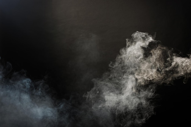 Bocanadas densas y esponjosas de humo blanco y niebla sobre fondo negro, nubes de humo abstractas, movimiento borroso fuera de foco. Golpes de fumar de la mosca de hielo seco de la máquina y revoloteando en el aire, textura de efecto