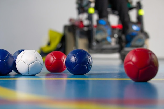 Boccia um homem deficiente sentado em uma cadeira de rodas perto de bolinhas por jogar bocha tricolor