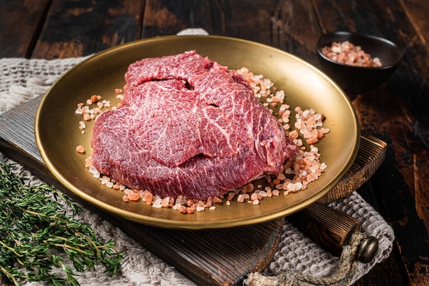 Bochechas de carne de vitela crua em chapa de aço com sal rosa Fundo de madeira Vista superior