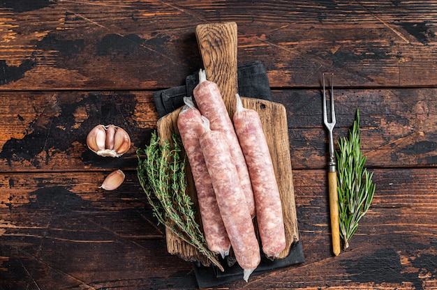 Bockwurst salsichas crus com carne de porco em uma placa de madeira. fundo de madeira escuro. vista do topo.