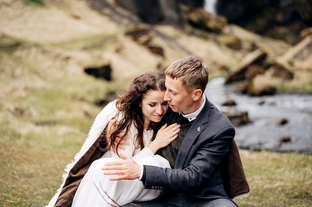 Boda de destino en Islandia, cerca de la cascada de Kvernufoss. Una pareja de novios se sienta a orillas de un