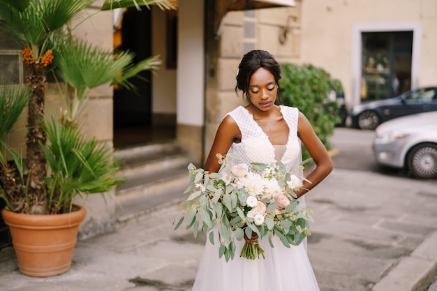 Boda en Florencia, Italia. Novia afroamericana con un vestido blanco y un velo largo. Con un magnífico ramo de la novia en sus brazos.
