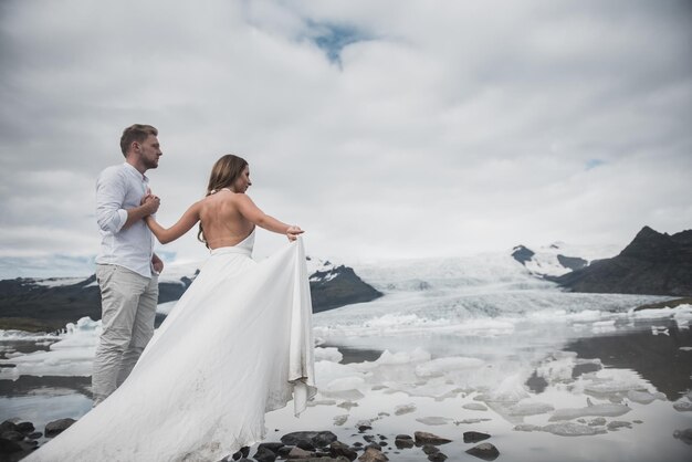 Boda en Islandia. Un chico y una chica con un vestido blanco se abrazan mientras están de pie sobre un hielo azul