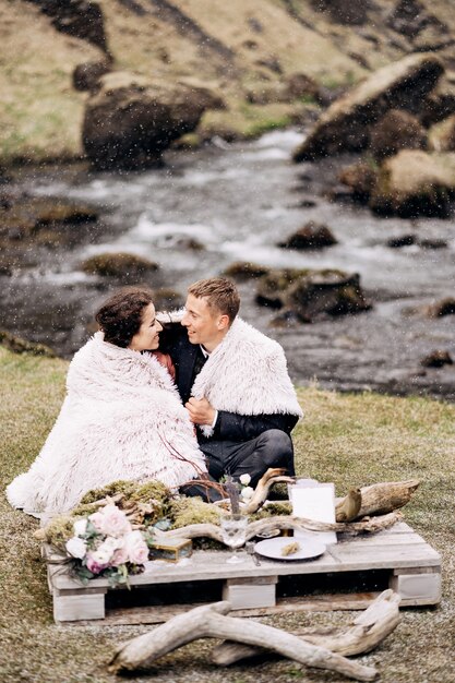 Boda en islandia de destino cerca de la cascada de kvernufoss una pareja de novios se sienta en las orillas de un