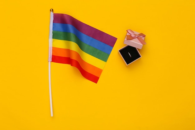 Boda LGBT. Bandera del arco iris LGBT y anillo en caja sobre fondo amarillo. Tolerancia, libertad