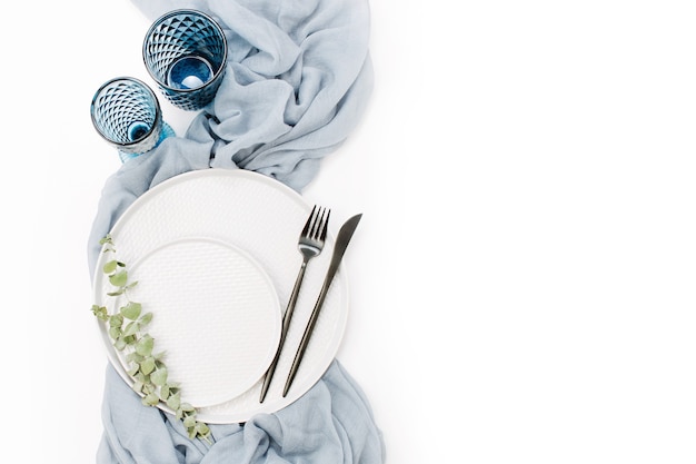 Boda o mesa festiva. Platos, copas de vino, velas y cubiertos con textil decorativo gris sobre fondo blanco. Hermoso arreglo.