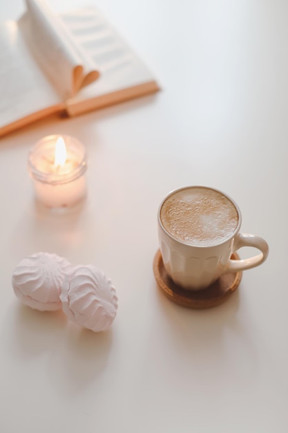 Bodegón acogedor con una taza de café, vela, libro abierto sobre un fondo soleado, decoración interior de la casa de primavera...