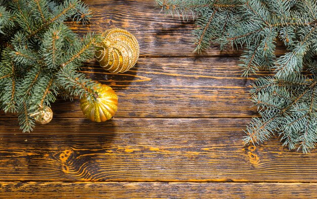 Bodegón de alto ángulo de ramas de pino decoradas con bolas de oro en la mesa de madera con patrón de grano rústico - Fondo de Navidad festivo con espacio para copiar texto