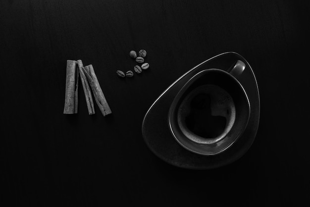 Bodegón de arriba hacia abajo en blanco y negro con taza de café espresso, palitos de canela y granos de café