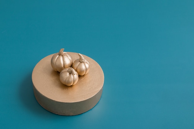 Bodegón de calabazas doradas en un podio sobre un fondo turquesa con espacio de copia. Concepto minimalista de cosecha, otoño.