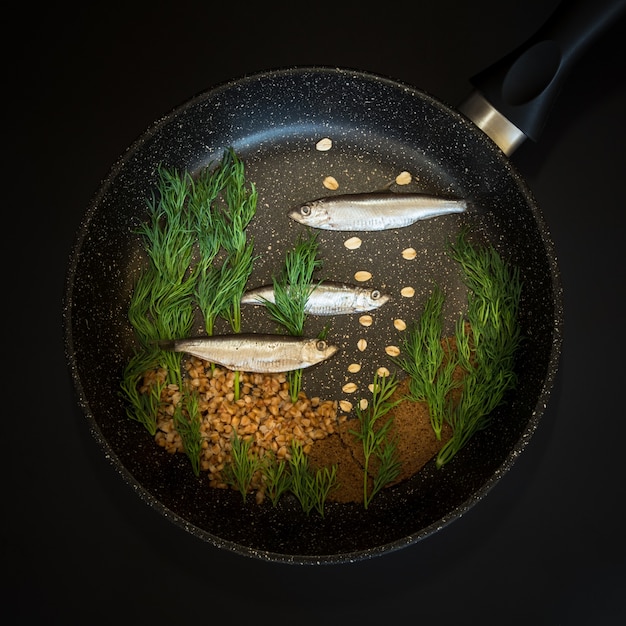 Foto bodegón creativo con peces pequeños, hierbas, trigo sarraceno y pan integral colocados en una sartén
