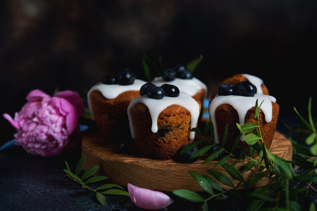 Bodegón de deliciosas magdalenas caseras vertidas con azúcar Fudge y decoradas con arándanos sobre un fondo oscuro.