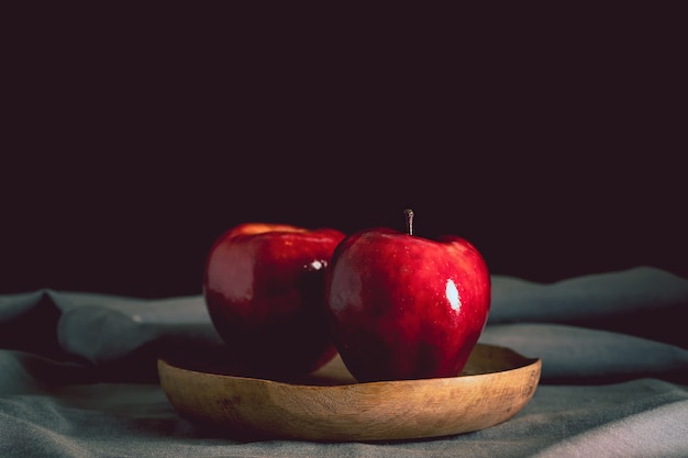 Foto bodegón de dos manzanas rojas sobre una placa de madera y un mantel gris