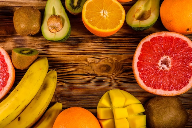 Foto bodegón con frutas exóticas plátanos mango naranjas aguacate pomelo y kiwis en mesa de madera rústica vista superior