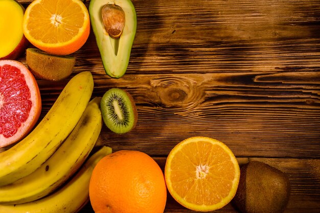 Bodegón con frutas exóticas Plátanos mango naranjas aguacate pomelo y kiwis en mesa de madera Vista superior