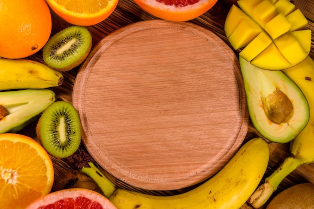 Bodegón con frutas exóticas y tabla de cortar Plátanos mango naranjas aguacate pomelo y kiwis en mesa de madera rústica Vista superior