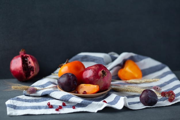 Bodegón de frutas de otoño. Granada, caqui y ciruela en mesa gris oscuro. Copia espacio
