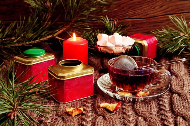 Bodegón de invierno cajas multicolores con té un colador malvaviscos aireados en un jarrón una vela encendida en un espacio de fondo oscuro para texto