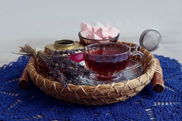 Bodegón de invierno una taza de té con un ramo de lavanda en una bandeja decorativa en una servilleta calada azul sobre un fondo gris