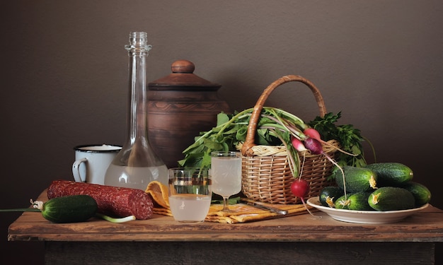 Bodegón con licor de luna, verduras frescas en la cesta y salchicha en un estilo rústico.