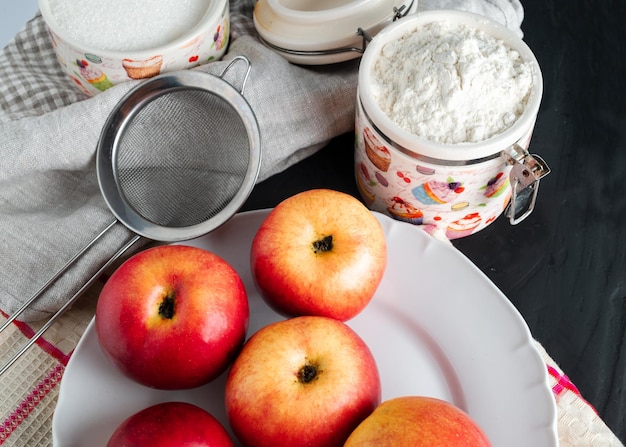 Foto bodegón con manzanas esparcidas sobre un plato paño de cocina y harina