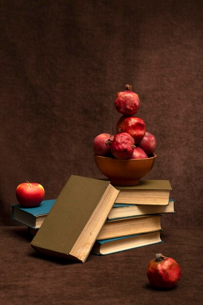 Bodegón con manzanas y granadas un plato marrón y una pila de libros
