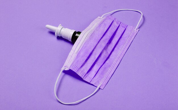 Bodegón médico sobre fondo morado. Mascarilla médica, spray nasal. Tratamiento frio. Minimalismo