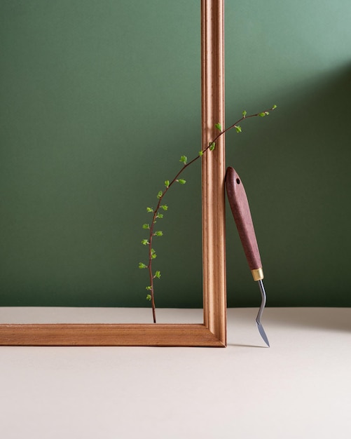 Bodegón minimalista con una rama verde de espátula y marco de madera