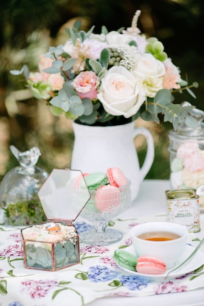 Foto bodegón novias mañana, plato con taza de té, copa de champán, anillos de boda y ramo de flores