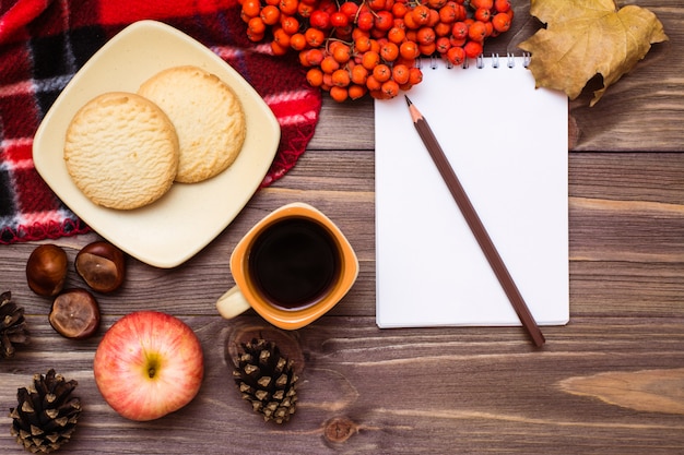 Bodegón otoñal: café, galletas, una tela escocesa, un cuaderno y un lápiz sobre madera