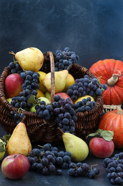 Bodegón otoñal con manzanas, uvas, calabaza y peras ubicadas sobre un fondo oscuro, cosecha de otoño, manzanas, peras y uvas en la cesta