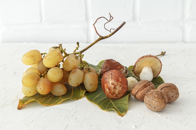 Bodegón otoñal con setas, hojas verdes y uvas.