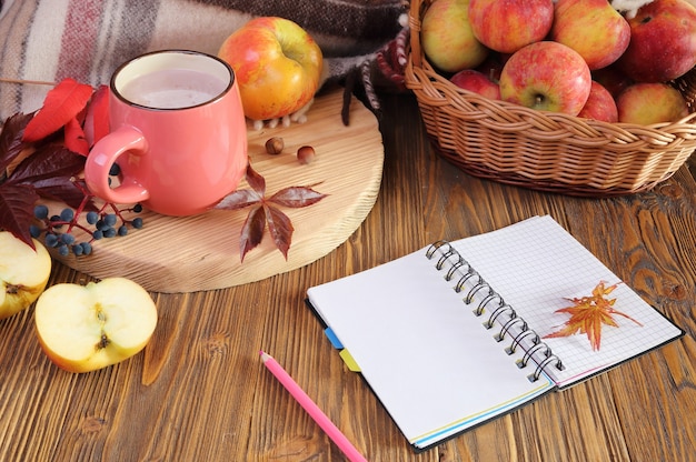 Bodegón otoñal con una taza de cacao, cuaderno y manzana.