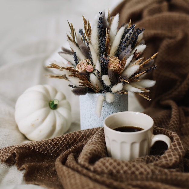 Bodegón otoñal con una taza de café con flores y calabazas en un acogedor plaid