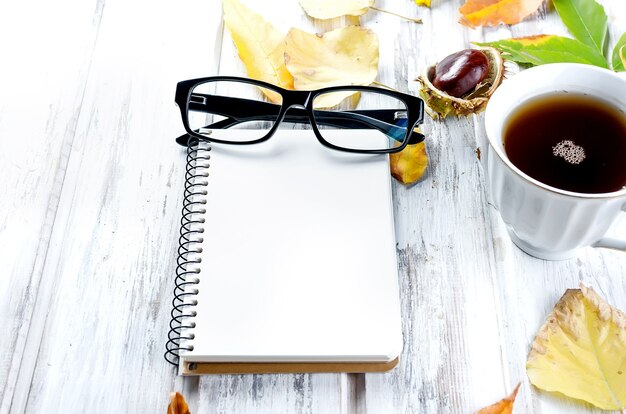 Foto bodegón otoñal con taza de té con galletas, cuaderno vacío, anteojos y hojas