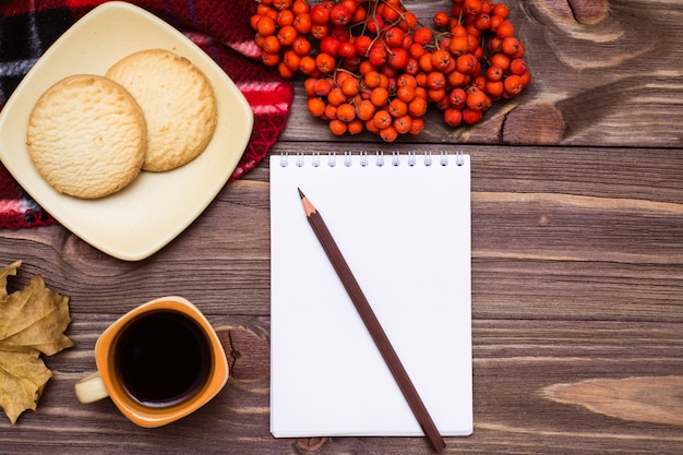 Bodegón de otoño café, galletas, un plaid, un cuaderno y un lápiz sobre madera Vista superior