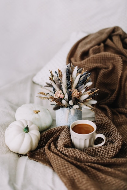 Bodegón de otoño con una taza de café con flores y calabazas en un acogedor plaid en la cama con estilo otoño ...