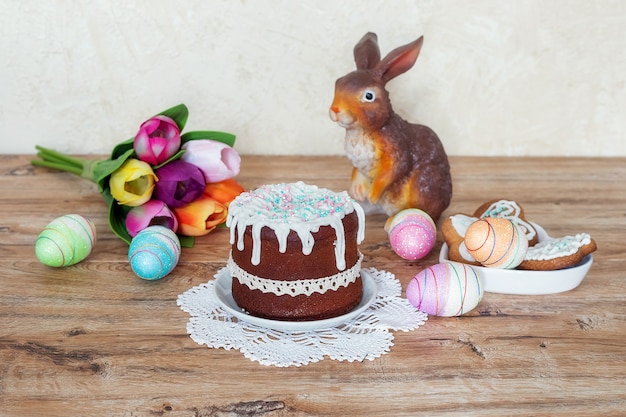 Bodegón de Pascua con pastel, galletas caseras, figura decorativa de conejo y huevos de Pascua en una mesa de madera. El concepto de celebrar la fiesta cristiana de Pascua.