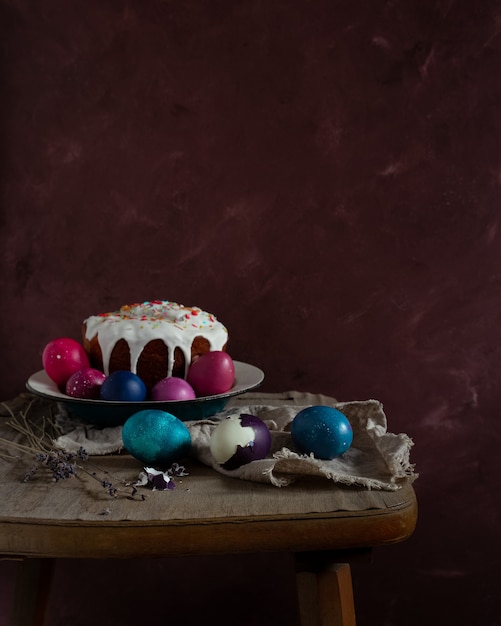 Bodegón con pastel de Pascua y huevos de colores sobre mesa rústica oscura