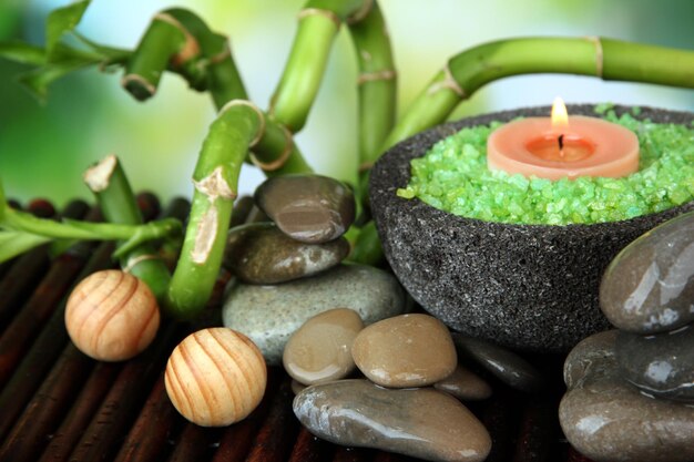 Bodegón con planta de bambú verde y piedras sobre estera de bambú sobre fondo brillante